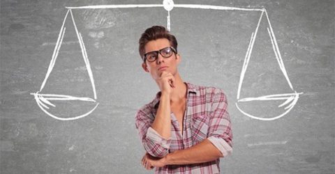 Young Man thinking infront of chalkboard with scale behind him