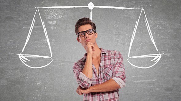 Young Man thinking infront of chalkboard with scale behind him