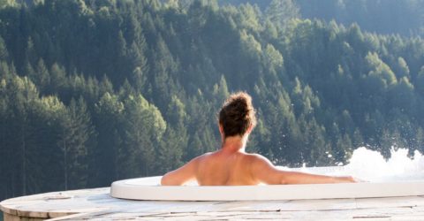 Topless woman enjoying view of forested mountain from hot tub