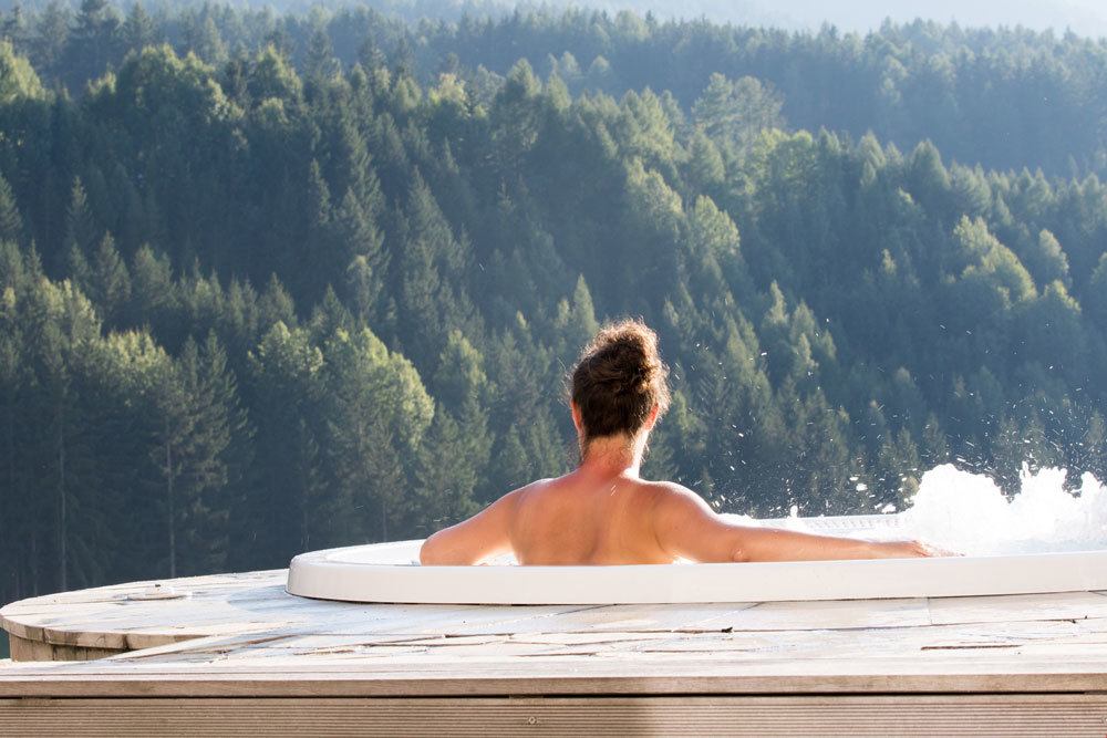 Topless woman enjoying view of forested mountain from hot tub