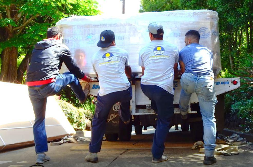 Four crew members unloading hot tub from flat bed truck.