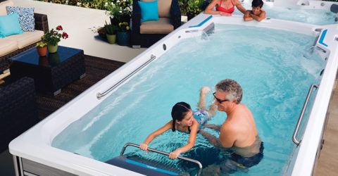 family of four swimming and lounging in an endless pool swim spa