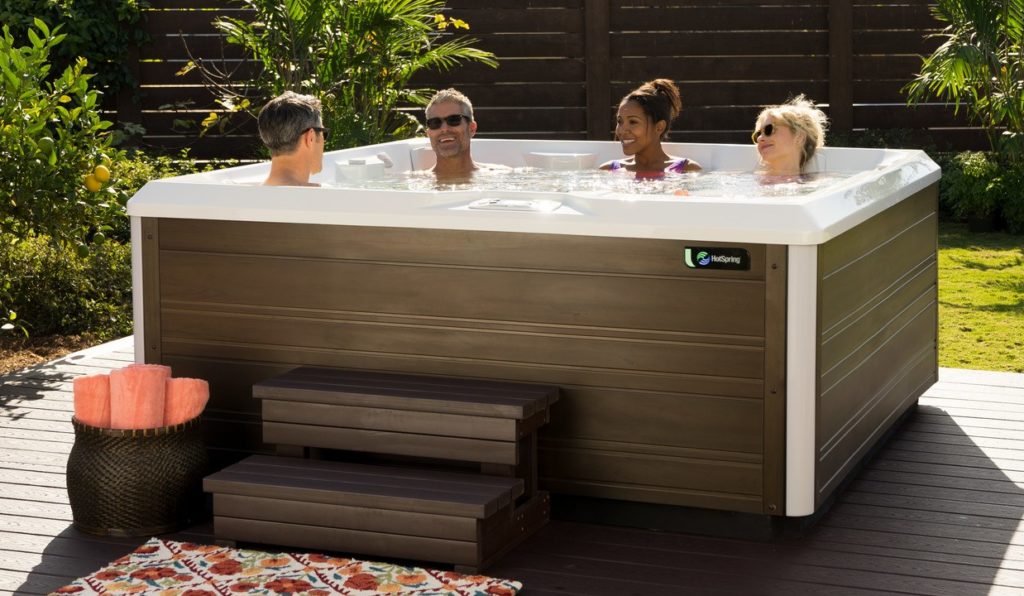 four people in a full size hot tub in backyard