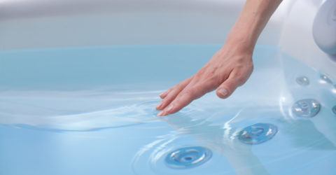 womans hand reaching into clean hot tub water