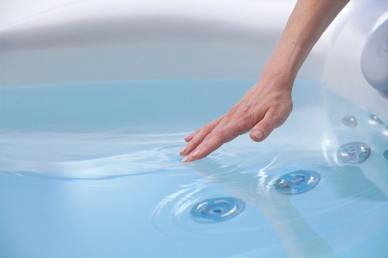 womans hand reaching into clean hot tub water