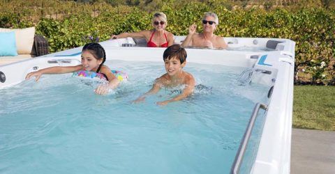 a family of two young children and a man a women enjoying swimming in a swim spa outside on a sunny day