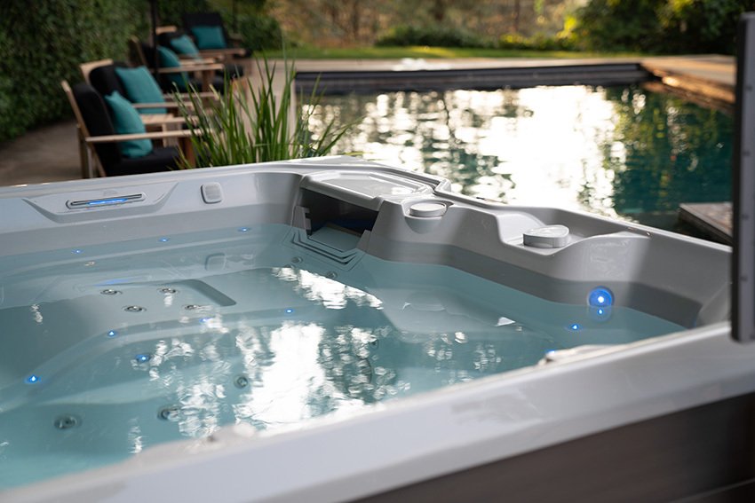 A Hot Spring Limelight Flair hot tub with a beautiful pool and patio furniture slightly out of focus in the background