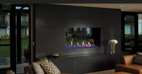 Davinci see-through gas fireplace insert on outside wall in condo complex with greenery seen through fireplace
