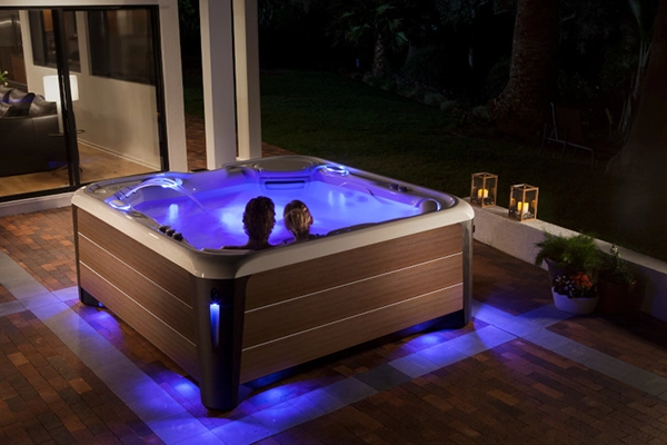 Couple soaking in a HotSpring Highlife at night with multi color LED lights illuminating the water and the surrounding deck