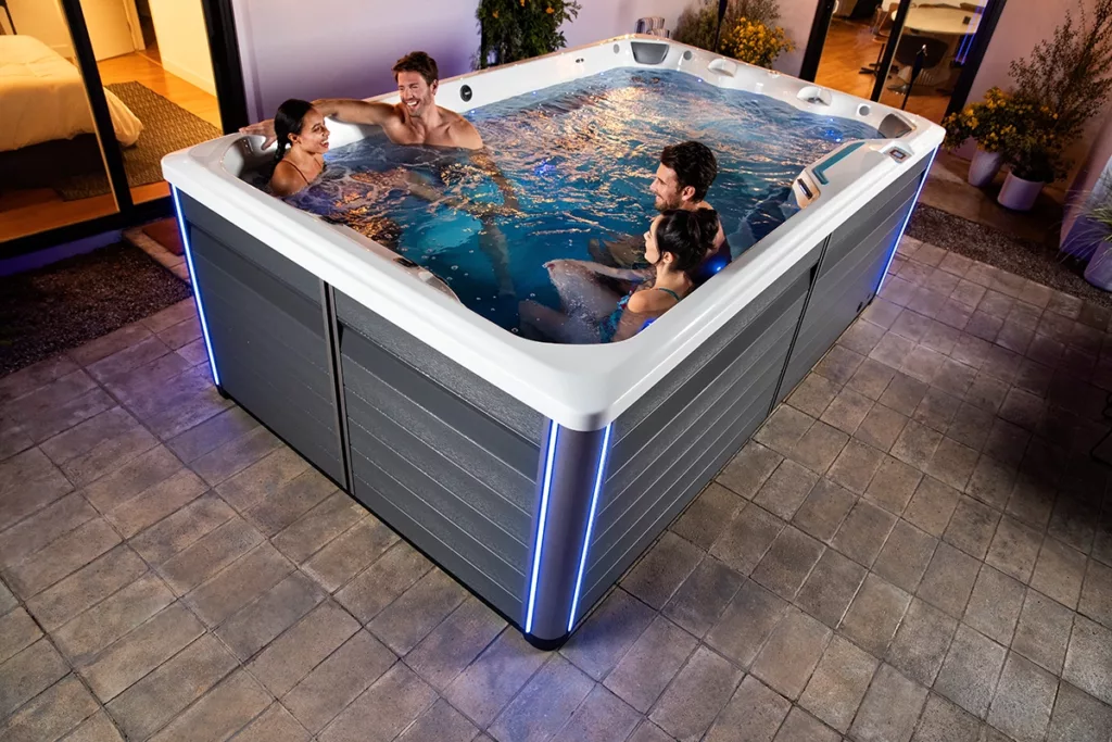 A smiling group of friends enjoys a swim spa in a small backyard space 