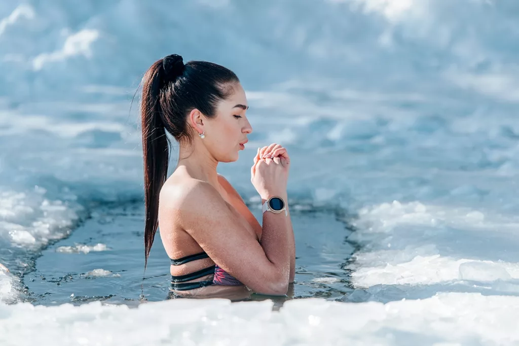 Women in bathing suit participating in cold plunge Cryotherapy in a partially frozen body of water for the medicinal health benefits.