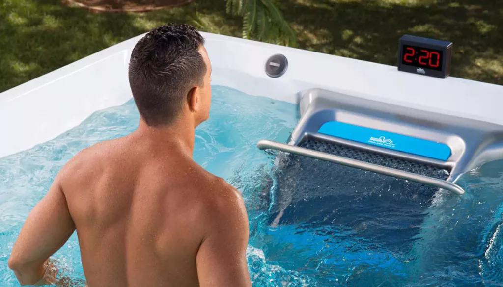 A man in an Endless Pools swim spa uses the Fit@Home® App with his pace display accessory.