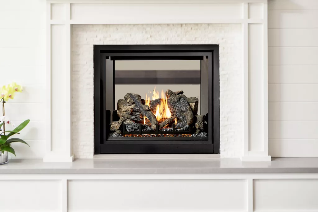 A lit gas fireplace with a white mantle and an orchid by the side.