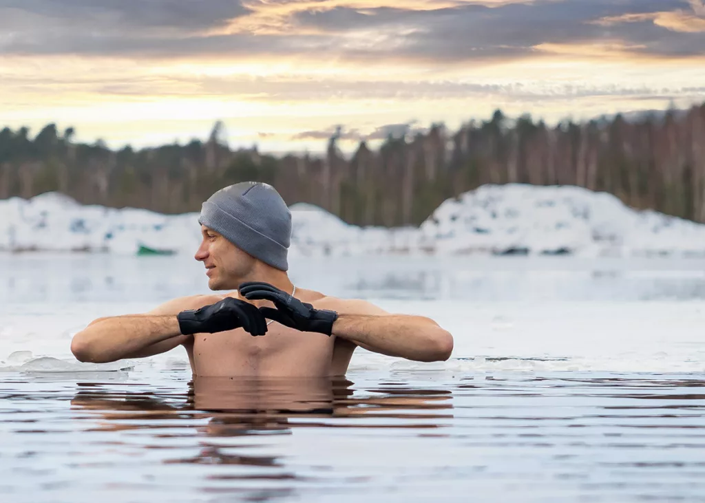 A young man in a beanie takes an ice bath outside.