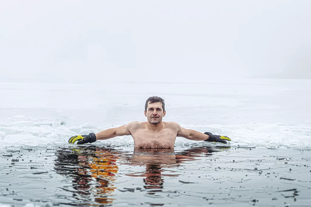 An athlete takes a cold plunge in an ice hole surrounded by snow