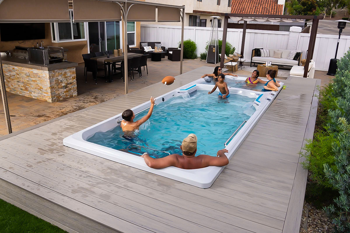 a group of people and kids play in the swim well of a swim spa, while more people relax in the spa end