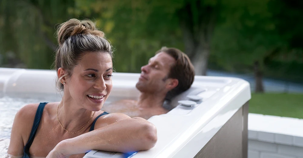 a young man and a woman in a navy blue swimsuit relax in a new hot tub outside without the jets running