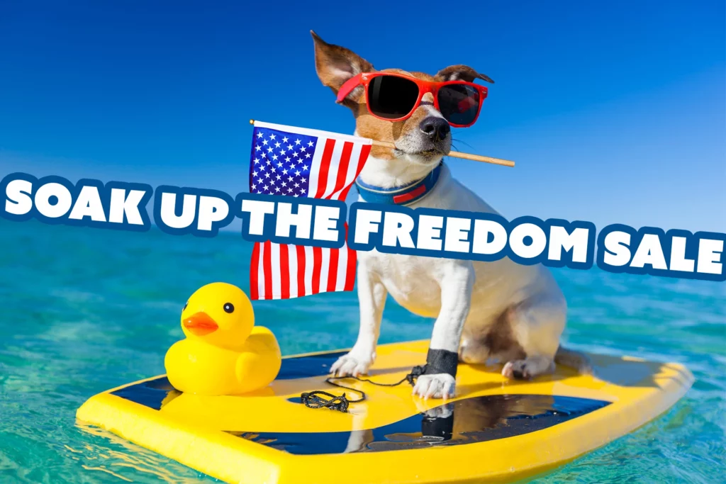 A dog on a boogie board holding an American Flag in it's mouth with text overall that reads "Soak Up the Freedom Sale"