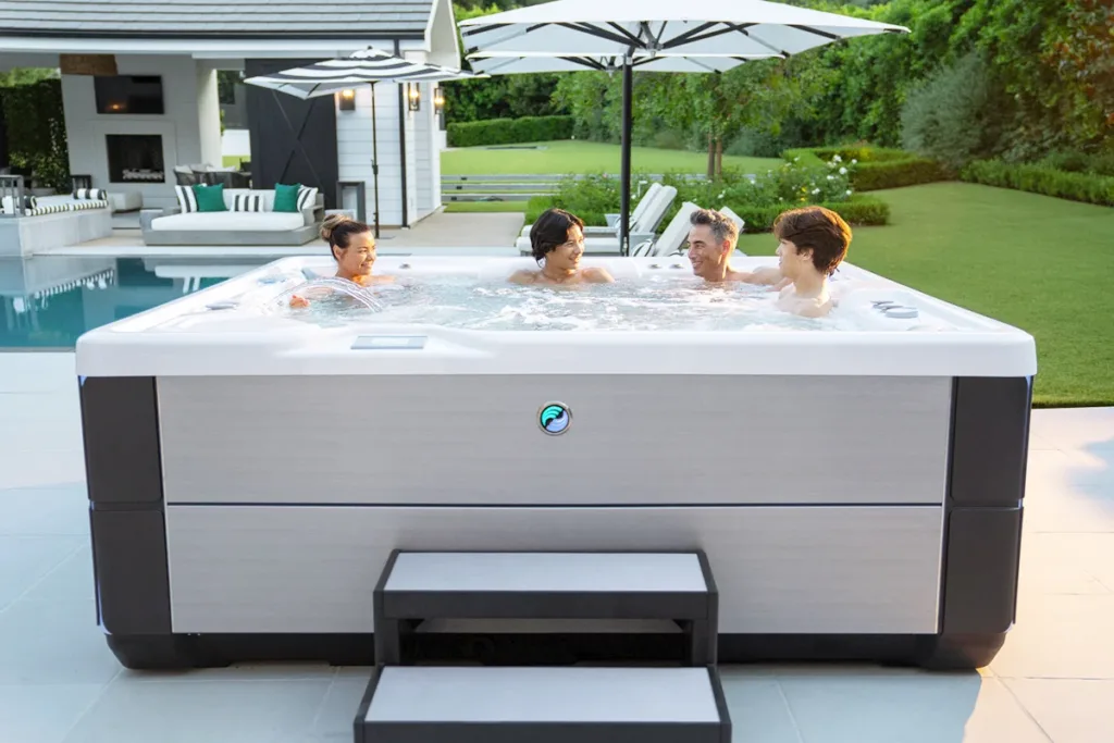 A smiling family relaxes in a Highlife Grandee hot tub by Hot Spring in a backyard