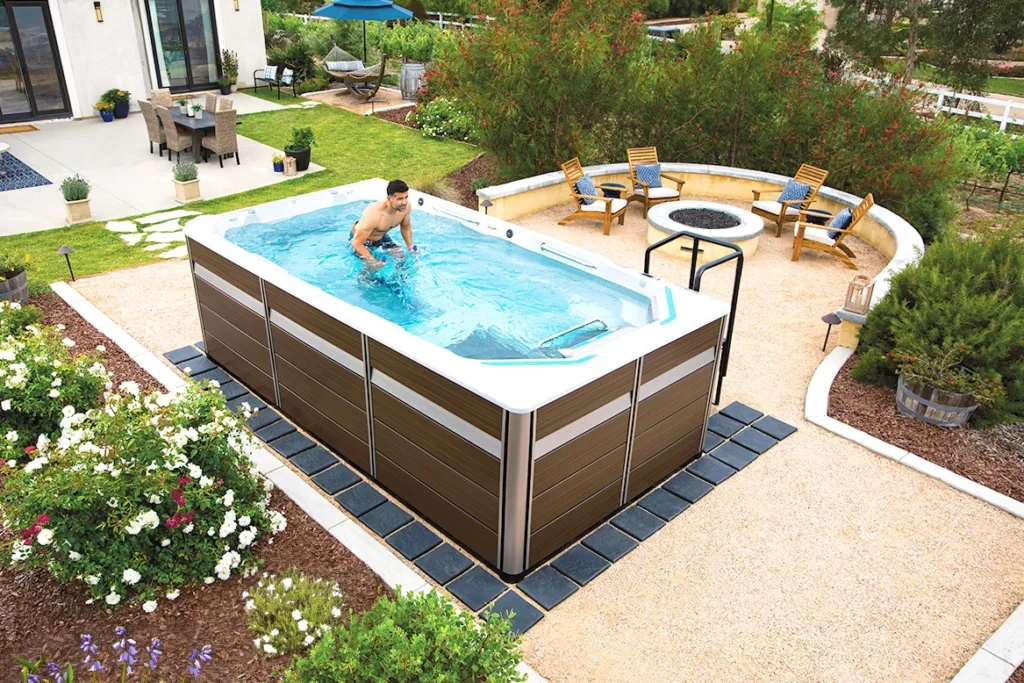 A man exercising in an Endless Pools fitness system swim spa, in a backyard filled with flowers