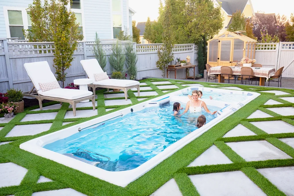 A smiling family swimming in an in-ground Endless Pools swim spa in their backyard