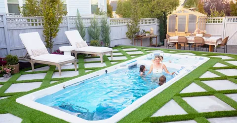 A smiling family swimming in an in-ground Endless Pools swim spa in their backyard
