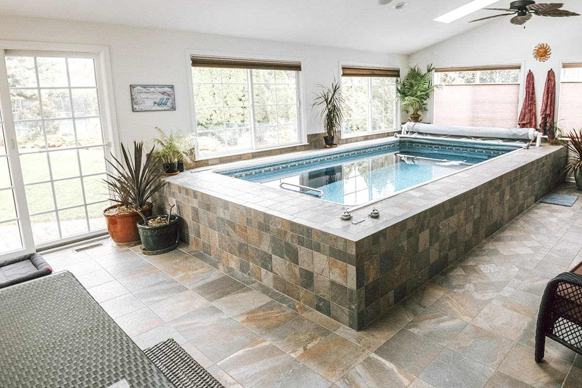 A custom designed modular pool inside a large room with white walls and windows, partially in-ground