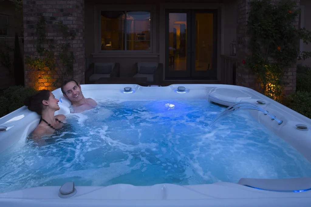 A smiling couple relaxes in an outdoor Hot Spring hot tub at night before bed